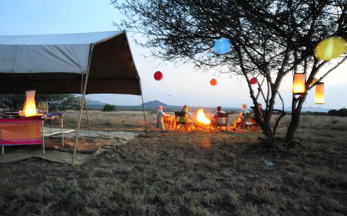 Evening camp setup with fire and hanging lanterns under acacia trees, Karisia Walking Safaris, Laikipia Highlands, Kenya