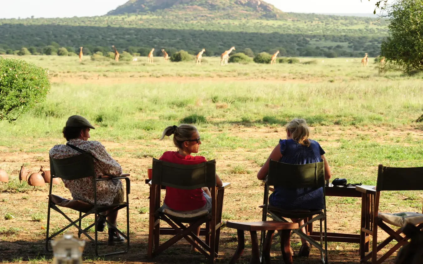 Guests seated on deck viewing giraffes in savanna landscape, Karisia Walking Safaris, Laikipia Highlands, Kenya
