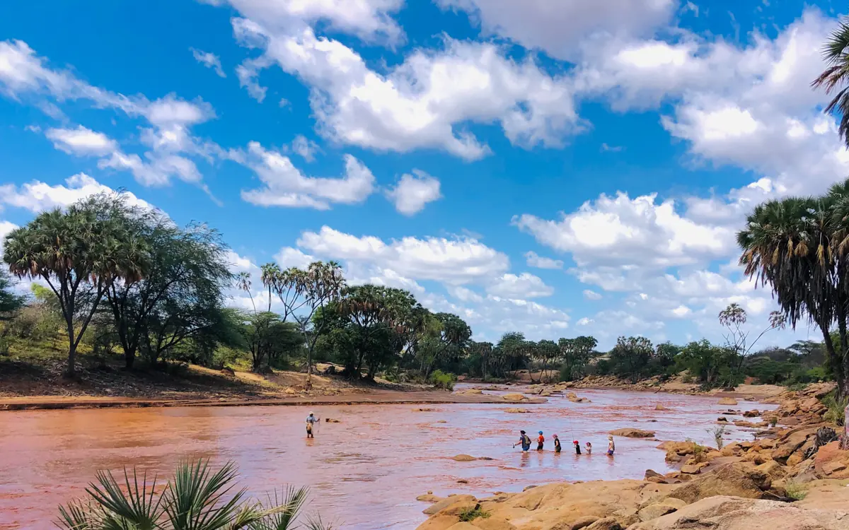 Red river with trees and people wading in water, Karisia Walking Safaris, Laikipia Highlands, Kenya