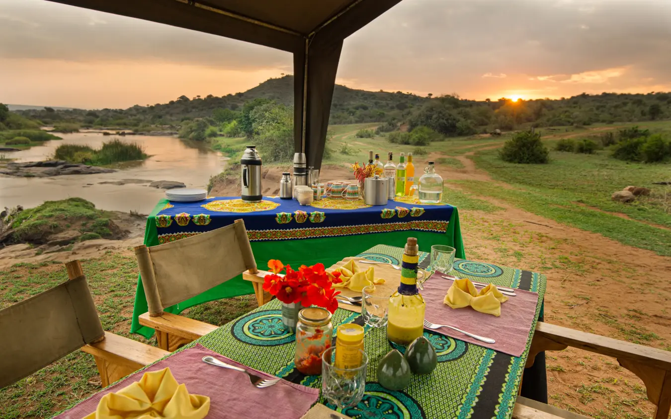 Dining setup on deck overlooking river and savanna at sunset, Laikipia Wilderness, Laikipia Highlands, Kenya