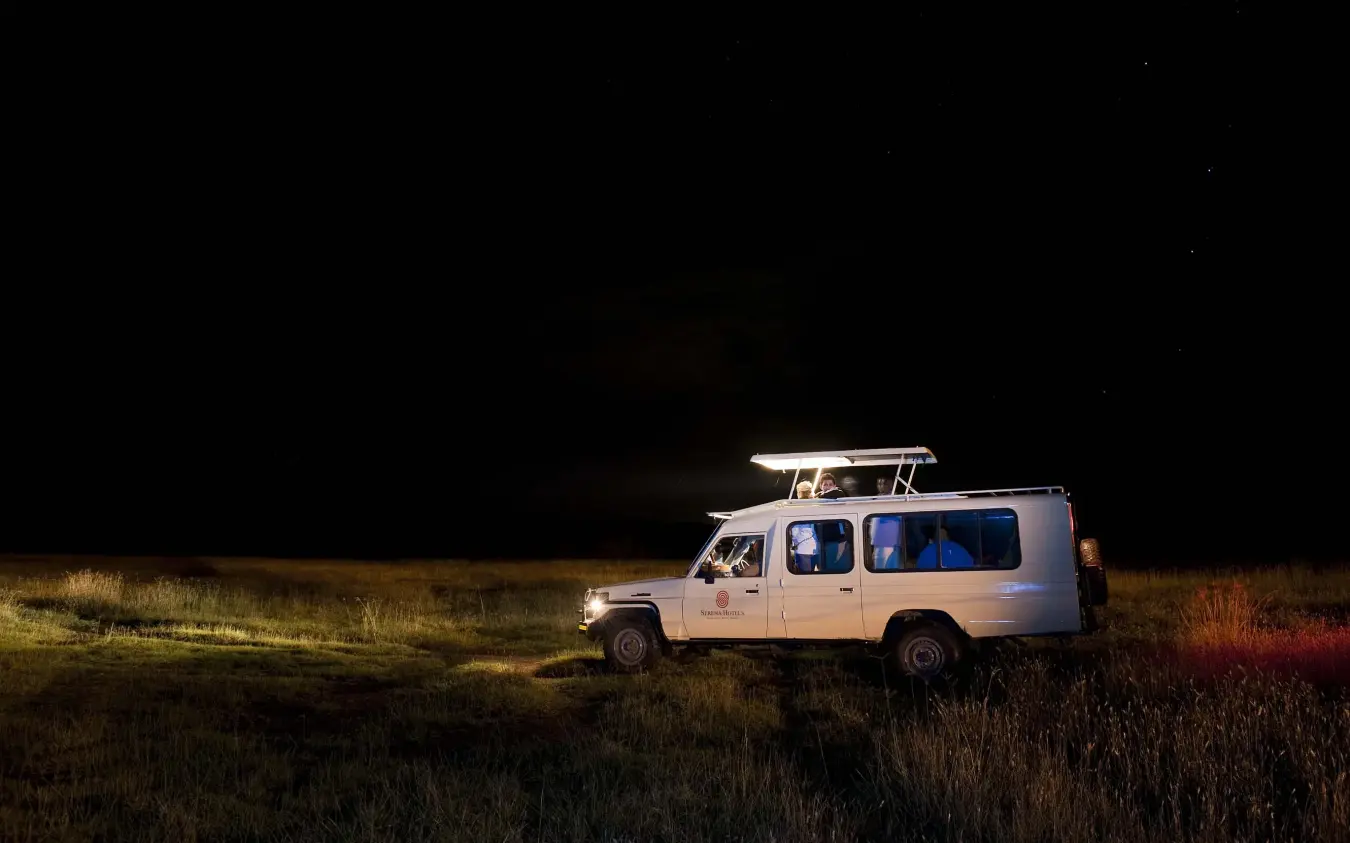 Safari vehicle illuminated on night game drive in grassland, Lake Elmenteita Serena Camp, Rift Valley Lakes, Kenya