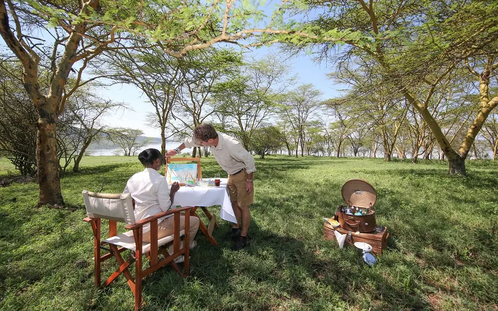 Couple dining at table under acacia trees beside lake, Lake Elmenteita Serena Camp, Rift Valley Lakes, Kenya