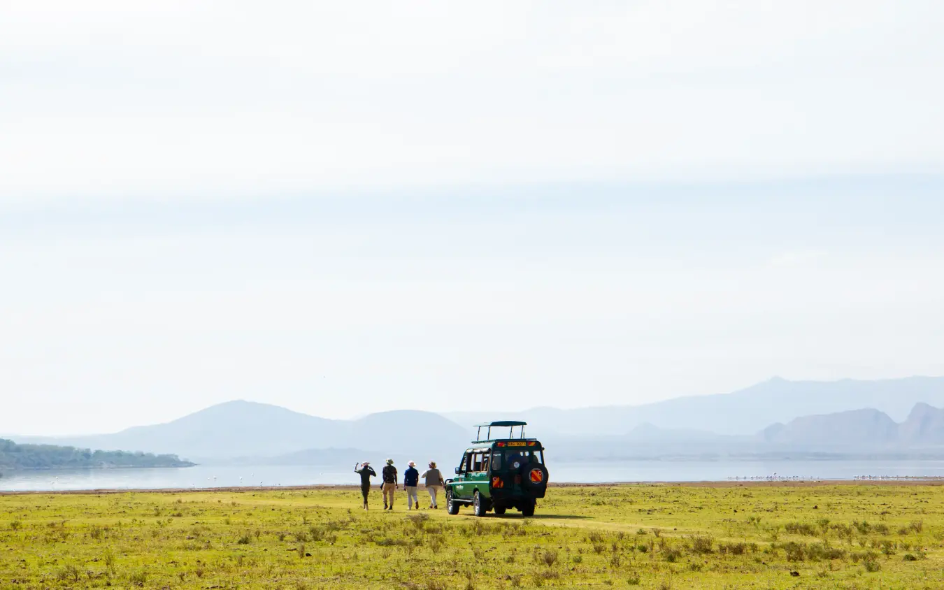 Safari vehicle with guests on grassland beside lake and mountains, Lake Elmenteita Serena Camp, Rift Valley Lakes, Kenya
