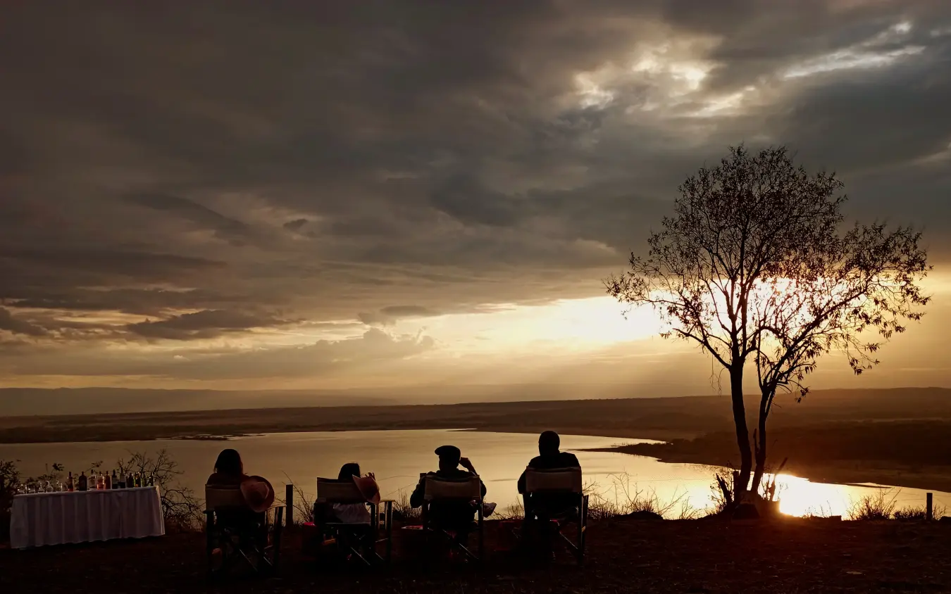 Silhouetted guests watching sunset over river valley from hillside camp, Lake Elmenteita Serena Camp, Rift Valley Lakes, Kenya