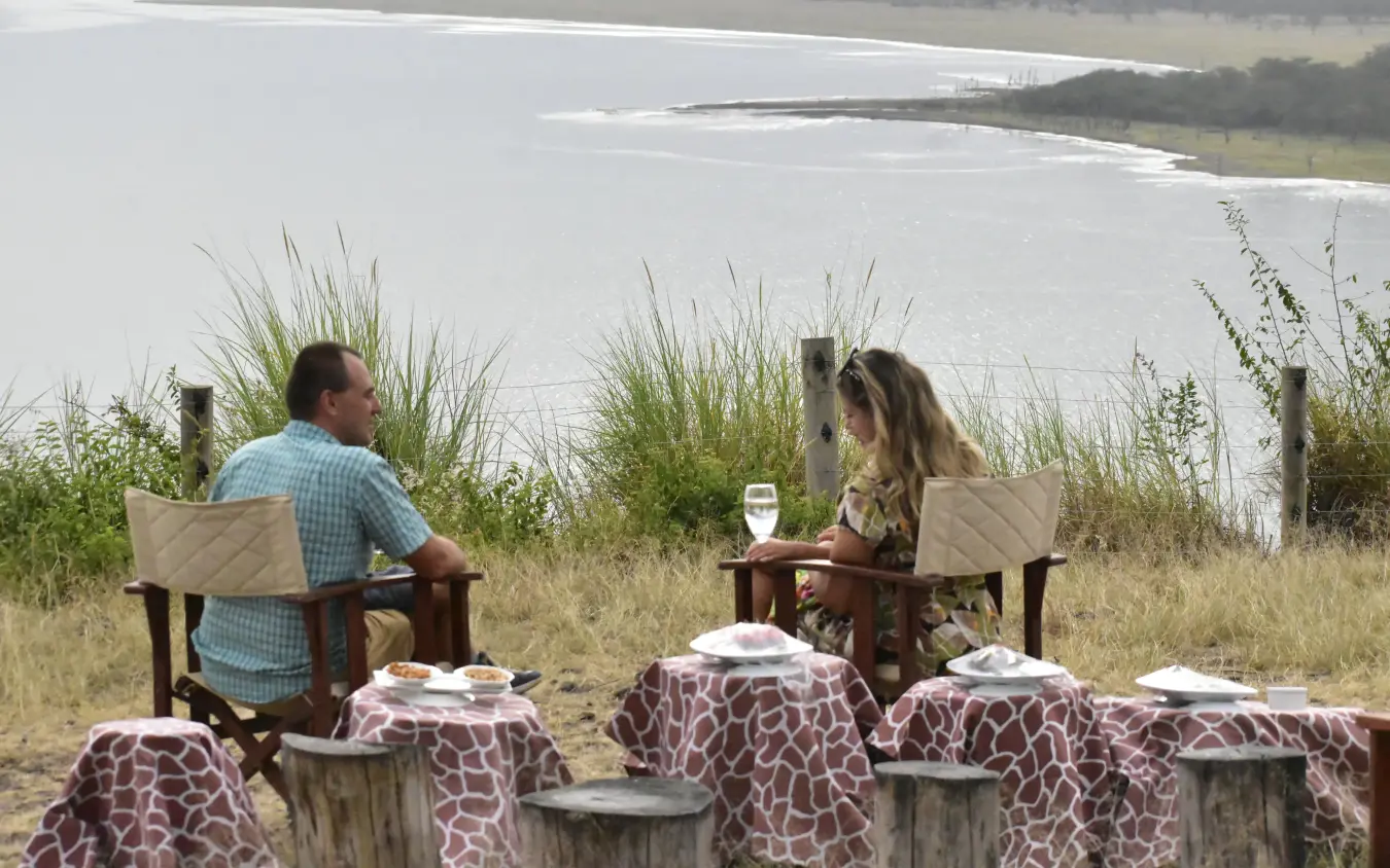 Couple relaxing in Adirondack chairs overlooking waterfront with coastal vegetation, Lake Elmenteita Serena Camp, Rift Valley Lakes, Kenya