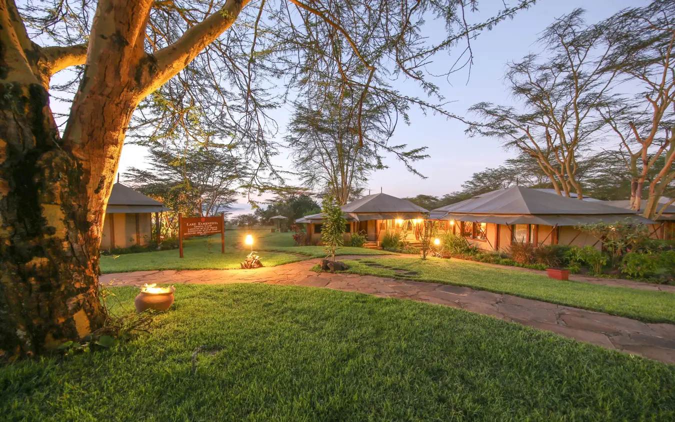 Luxury lodge courtyard with acacia trees and outdoor fire pit at dusk, Lake Elmenteita Serena Camp, Rift Valley Lakes, Kenya