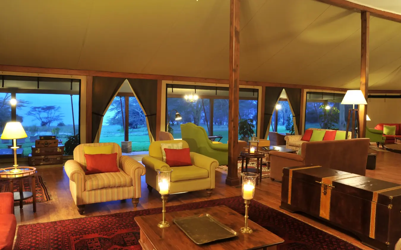 Open-plan lodge interior with floor-to-ceiling windows overlooking dusk landscape, Lake Elmenteita Serena Camp, Rift Valley Lakes, Kenya