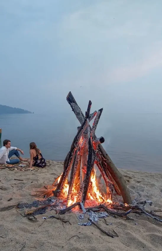 Couple enjoying bonfire on beach at dusk with water view, Lake Kivu Serena Hotel, Lake Kivu, Rwanda