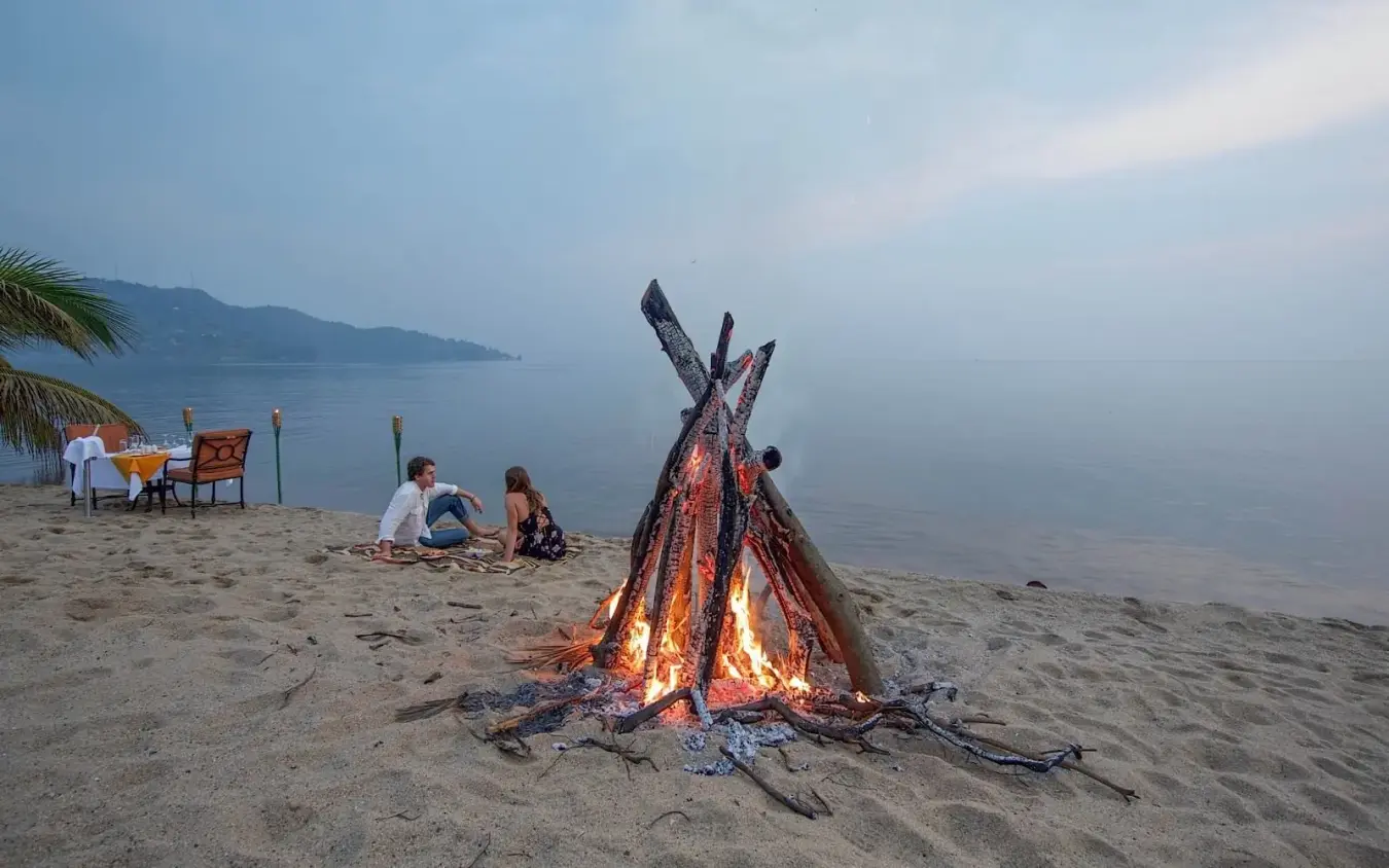 Couple enjoying bonfire on beach at dusk with water view, Lake Kivu Serena Hotel, Lake Kivu, Rwanda