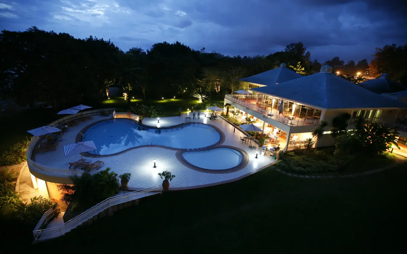 Illuminated resort pool complex with blue canopy at dusk surrounded by woodland, Lake Kivu Serena Hotel, Lake Kivu, Rwanda