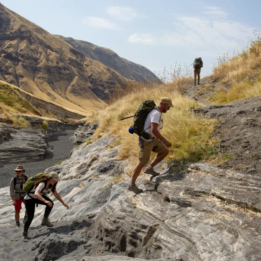 Hikers ascending rocky slopes above a river valley, Lake Natron Camp, Lake Natron, Tanzania