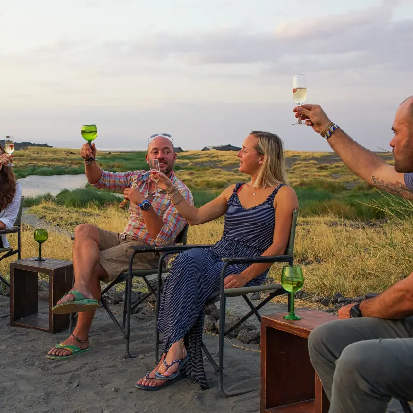 Guests toasting drinks at outdoor camp gathering, Lake Natron, Tanzania