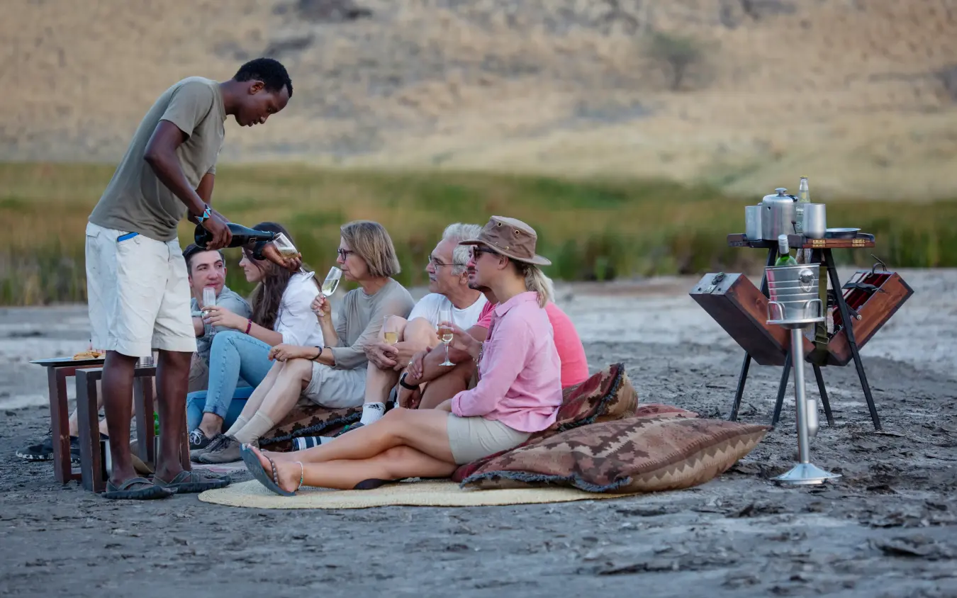 Guide serves drinks to guests during lakeside sundowner gathering, Lake Natron Camp, Lake Natron, Tanzania