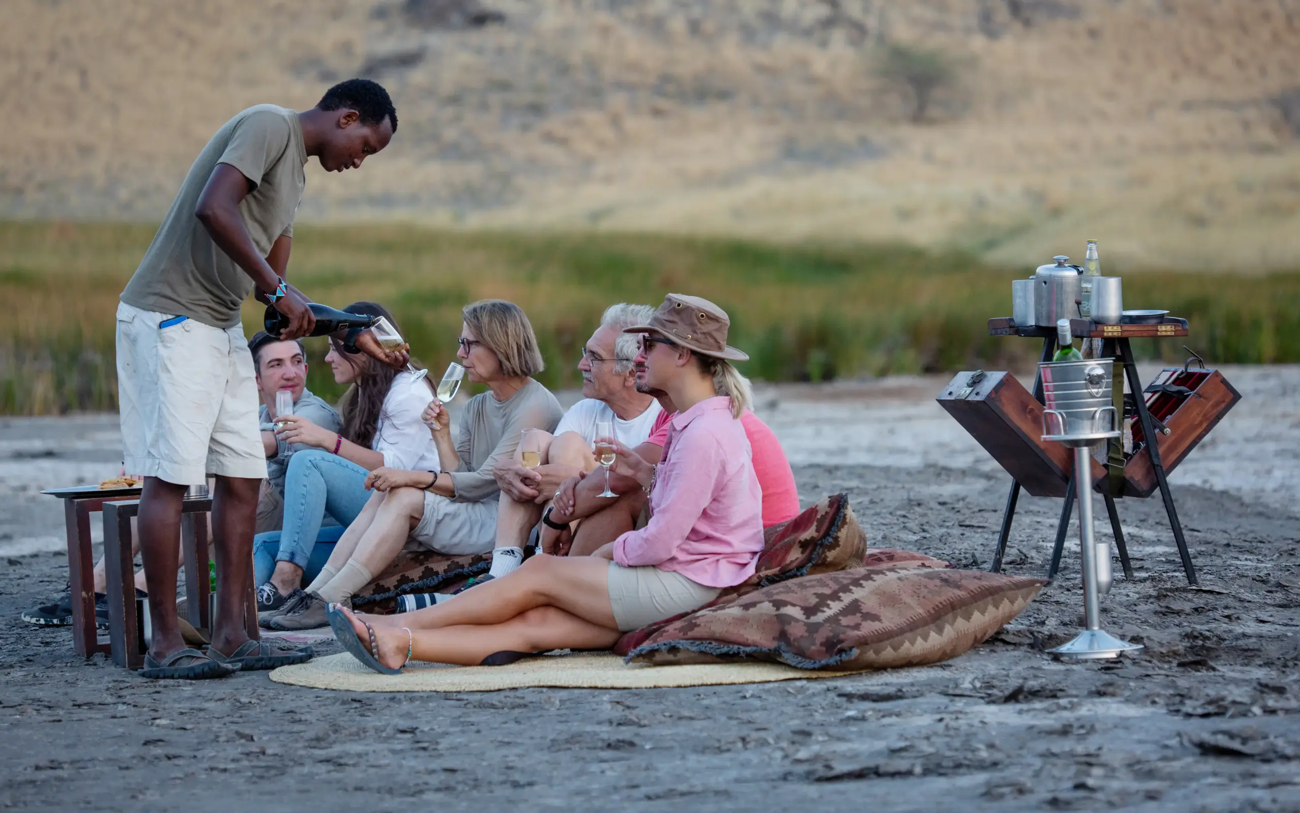 Guide serves drinks to guests during lakeside sundowner gathering, Lake Natron Camp, Lake Natron, Tanzania