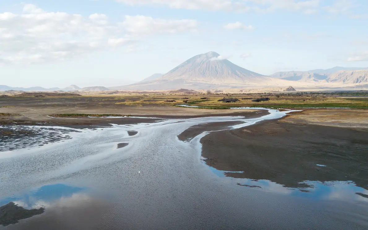 Winding river through volcanic landscape with mountain backdrop, Lake Natron Camp, Lake Natron, Tanzania
