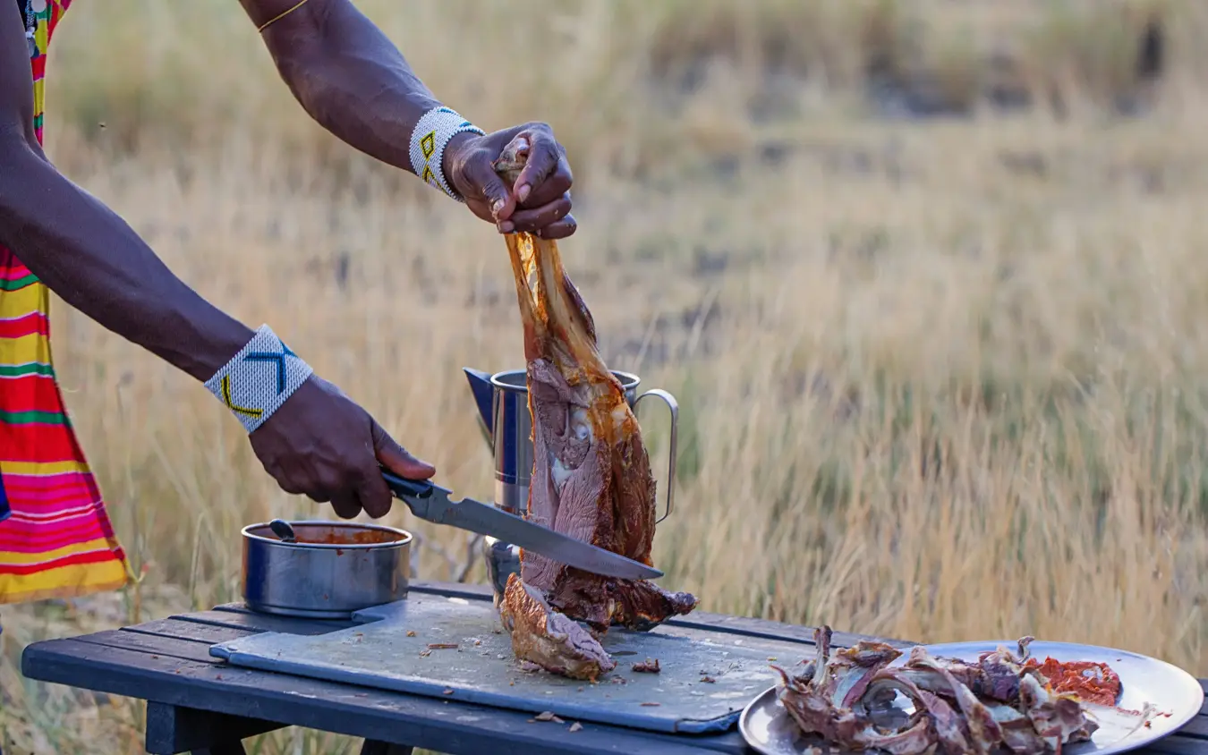 Cook preparing grilled meat over outdoor table, Lake Natron Camp, Lake Natron, Tanzania