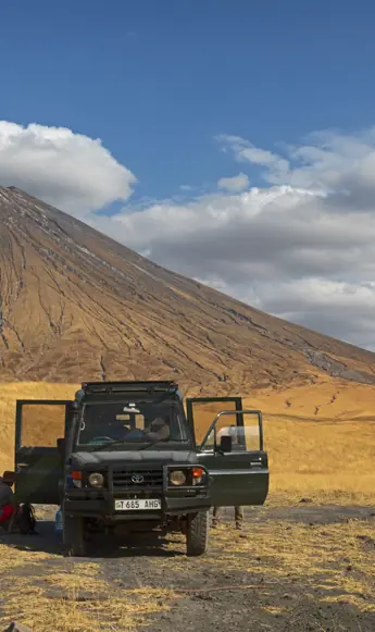 Jeep and hikers on golden plains with volcanic mountain, Lake Natron Camp, Lake Natron, Tanzania
