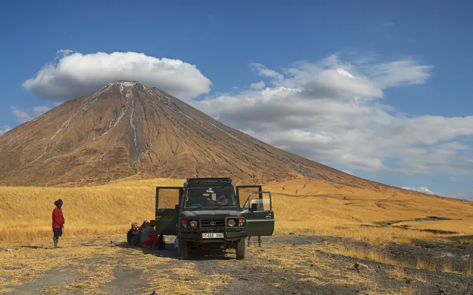 Jeep and hikers on golden plains with volcanic mountain, Lake Natron Camp, Lake Natron, Tanzania