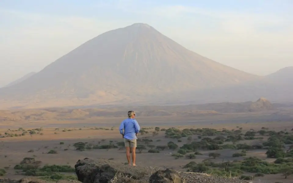 Runner pausing on rocky outcrop overlooking volcanic landscape, Lake Natron Camp, Lake Natron, Tanzania