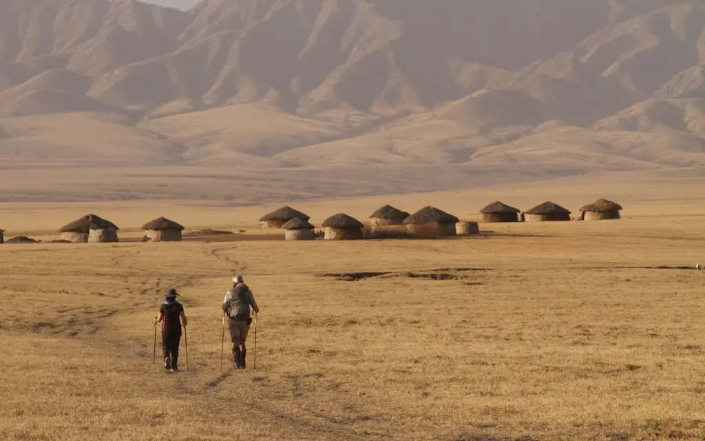 Two hikers walking across vast arid plains toward distant village, Lake Natron Camp, Lake Natron, Tanzania