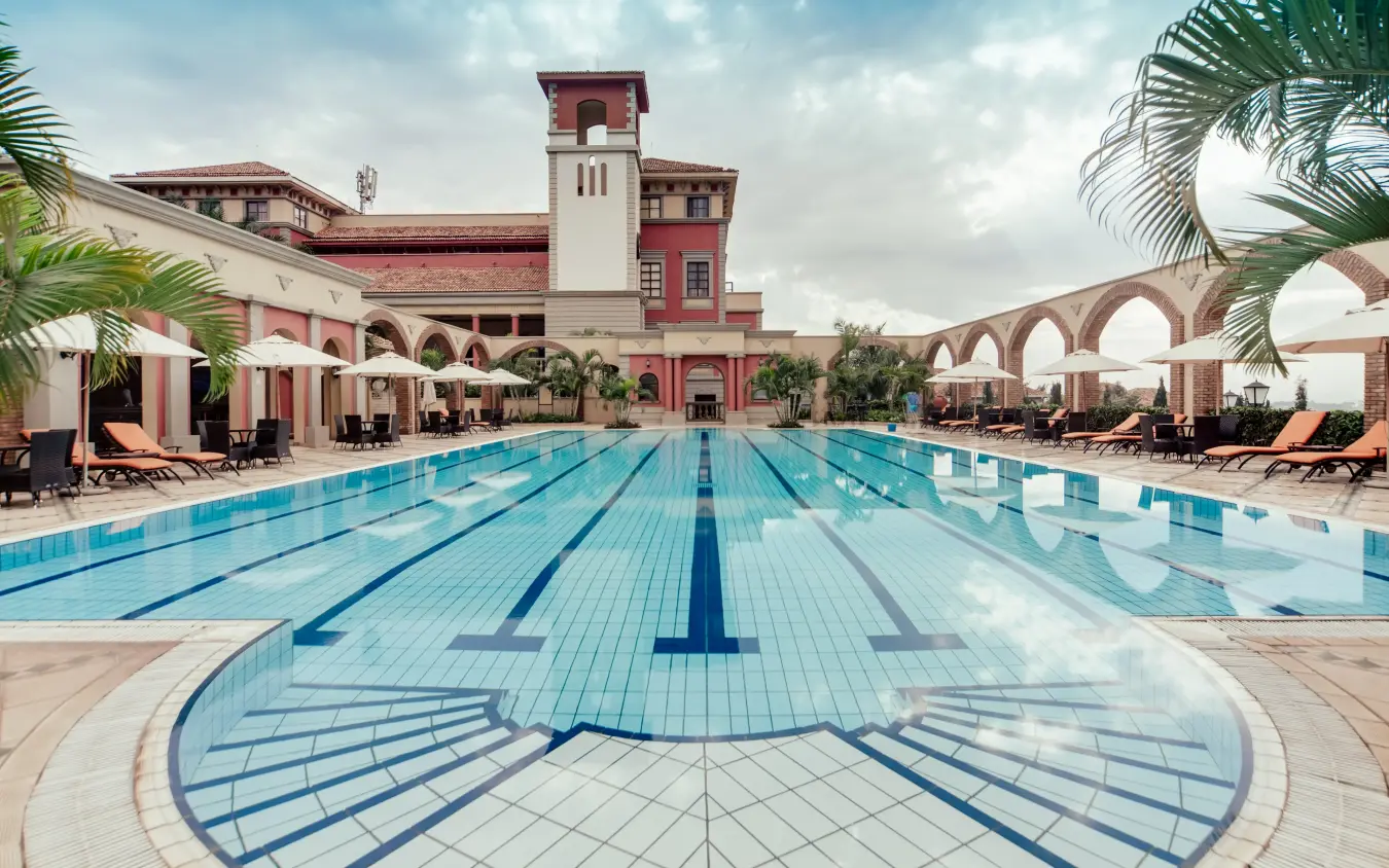 Olympic-length swimming pool with colonial-style lodge building and palm trees, Lake Victoria Serena Golf Resort & Spa, Entebbe and Kampala, Uganda