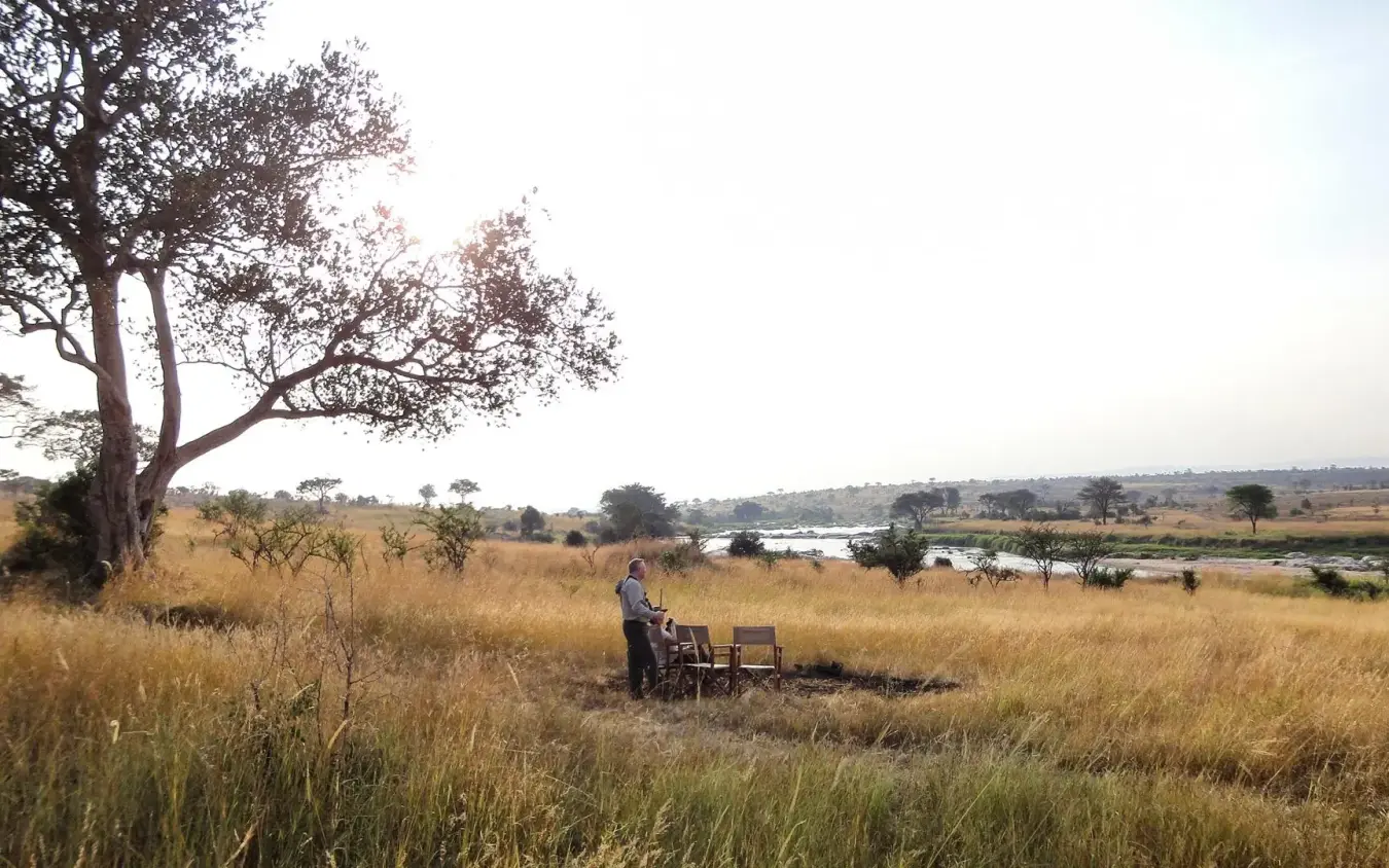 Guest dining at table in savanna landscape with river, Serian Serengeti Lamai, Serengeti National Park, Tanzania