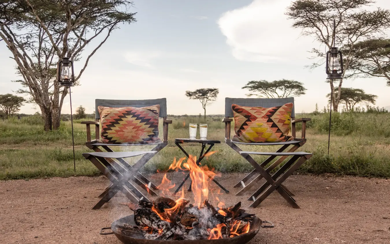 Campfire seating area with two director chairs and burning fire, Nyasi Tented Camp, Serengeti National Park, Tanzania