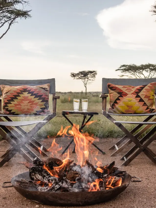 Campfire seating area with two director chairs and burning fire, Nyasi Tented Camp, Serengeti National Park, Tanzania