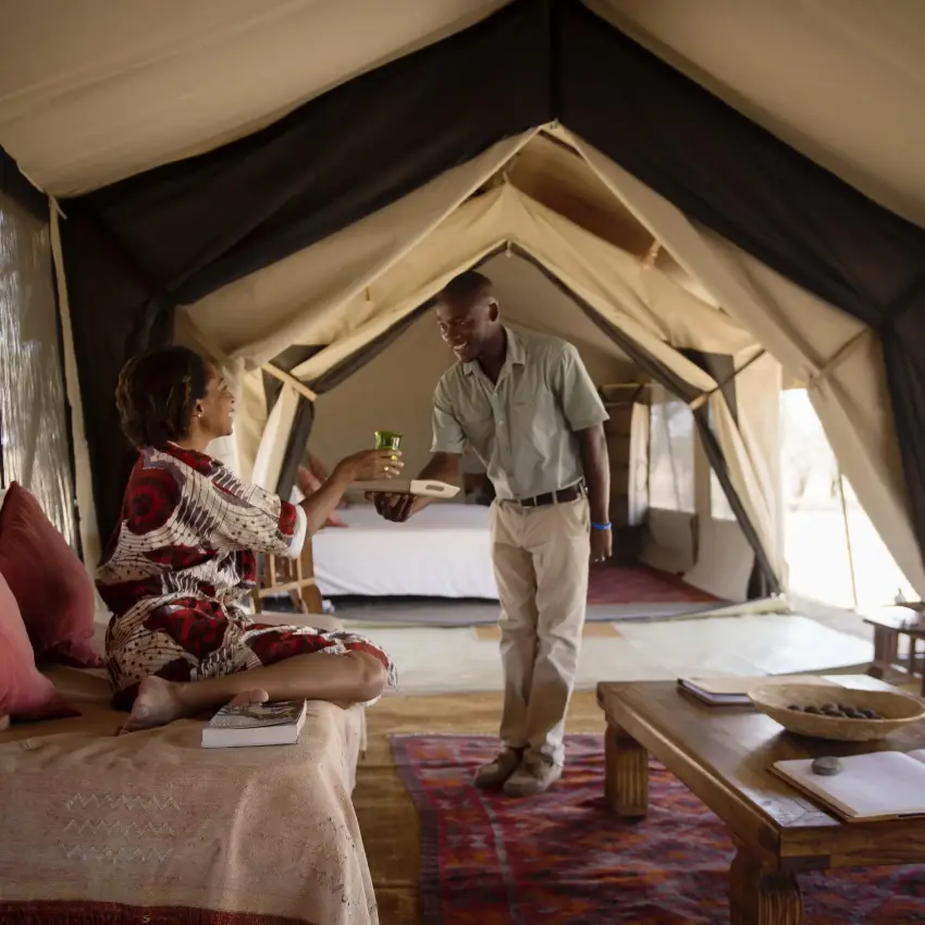 Woman and man inside luxurious canvas safari tent bedroom, Serian Serengeti Lamai, Serengeti National Park, Tanzania