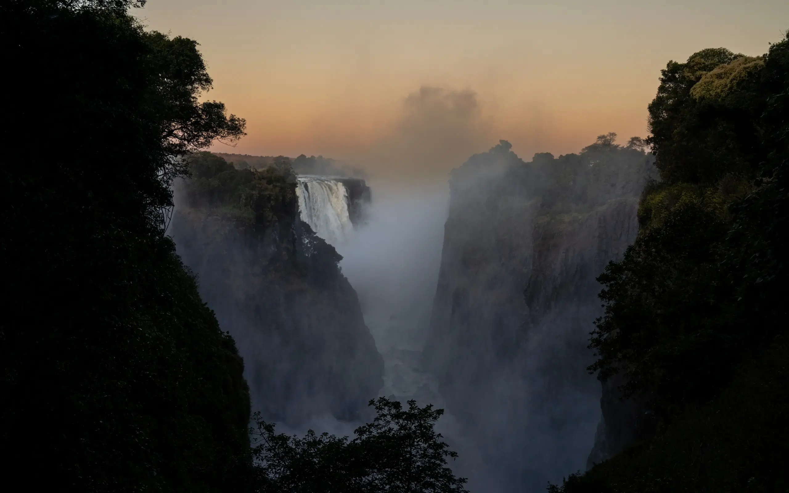 Misty waterfall cascading between forested cliff faces at dawn