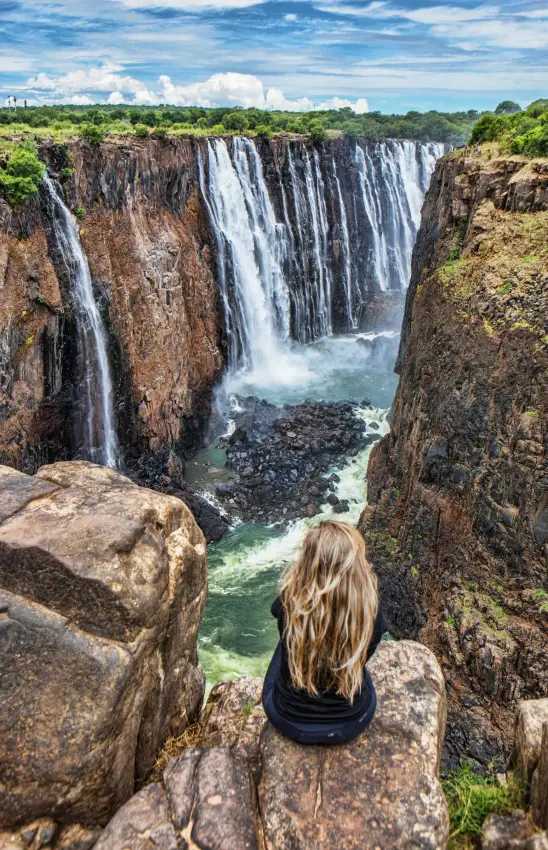 Woman sitting on rocky outcrop overlooking cascading waterfall