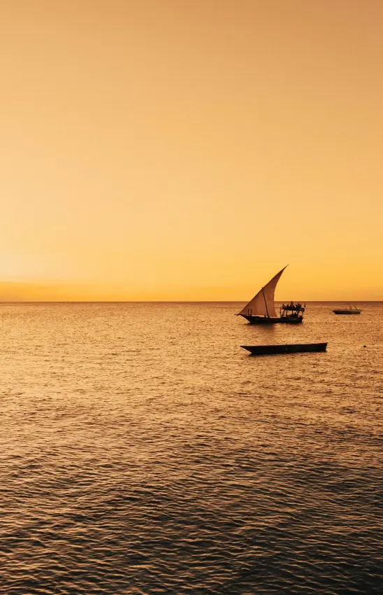 Traditional dhow sailboat silhouetted against a golden ocean sunset