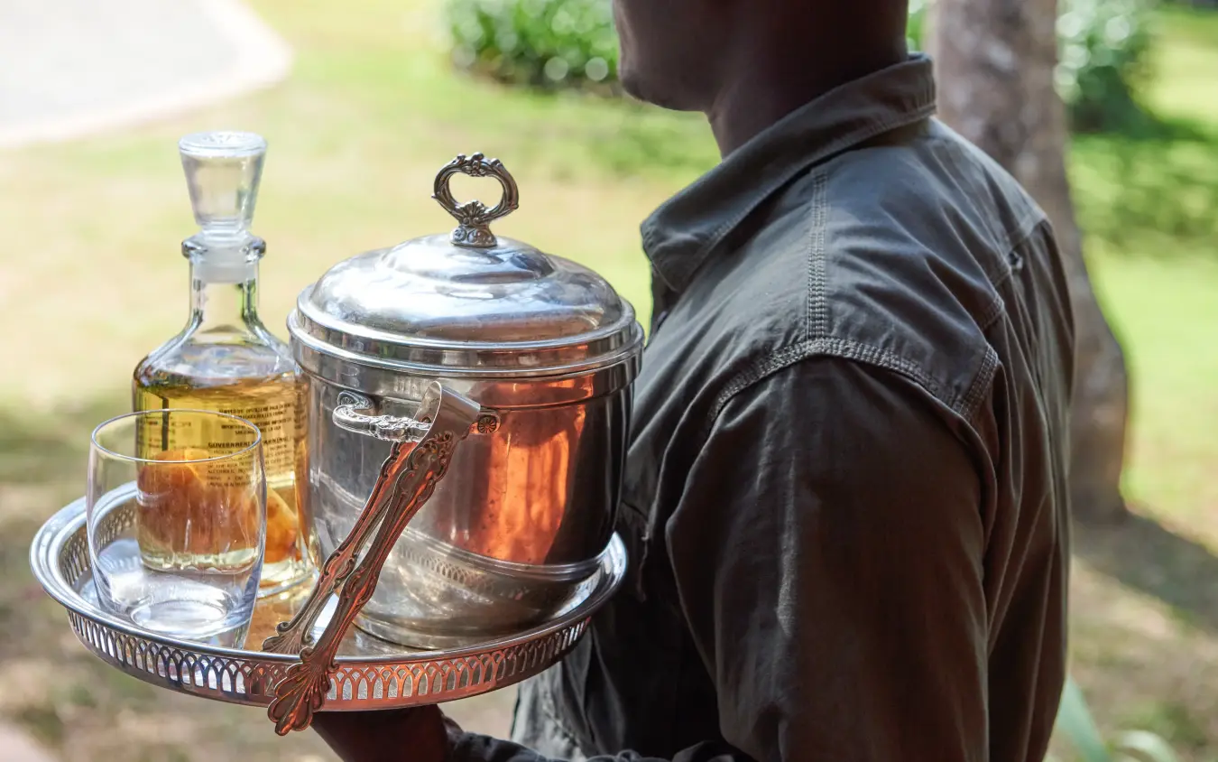 Server carrying silver teapot and glasses on tray outdoors, Legendary Lodge, Arusha, Tanzania