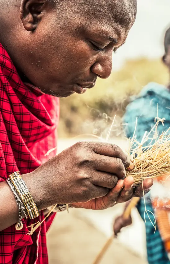 Local guide demonstrating traditional fire-making technique with dry grass, Mpingo Ridge Lodge, Tarangire National Park, Tanzania