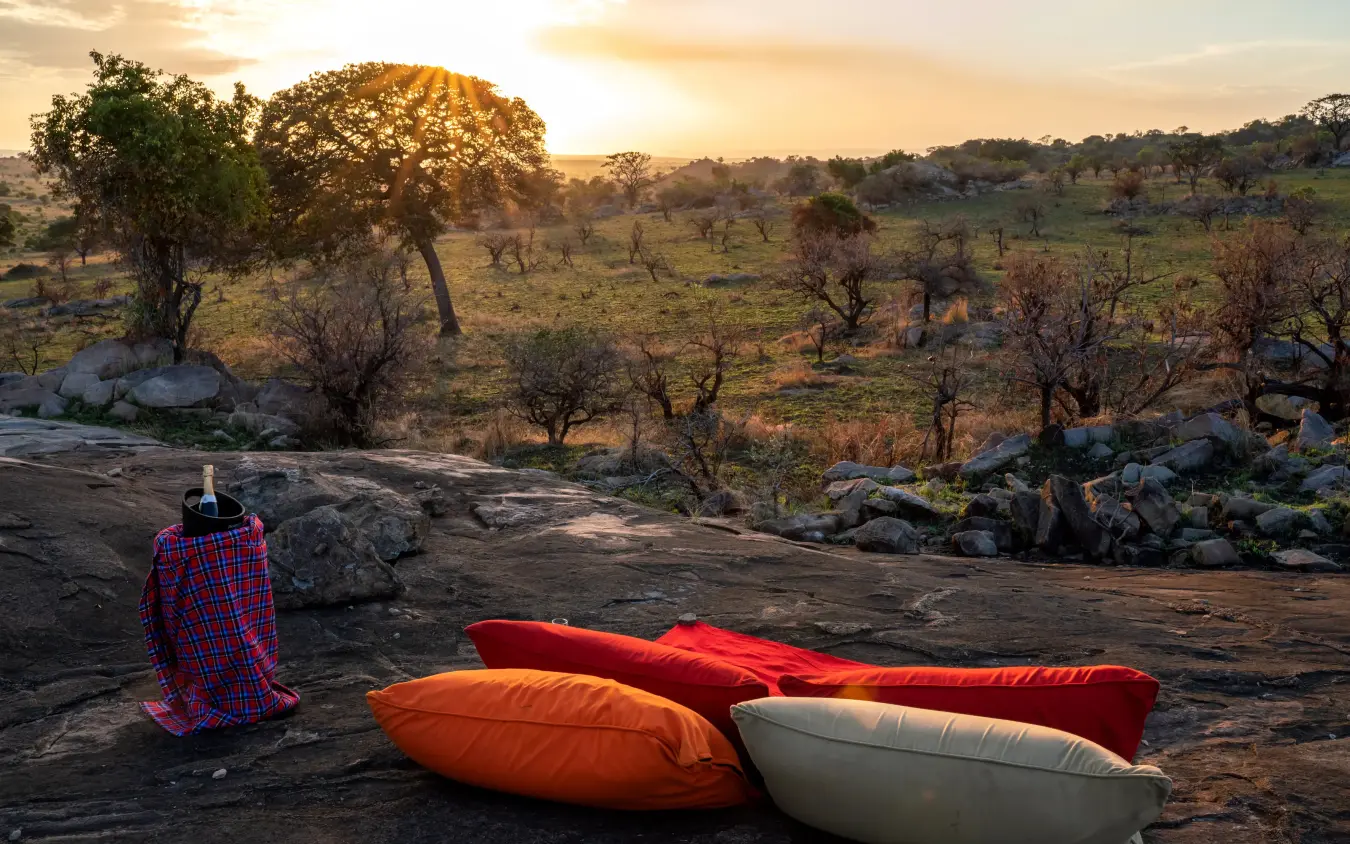 Person in traditional red blanket with sleeping bags at sunrise overlooking savanna, Mpingo Ridge Lodge, Tarangire National Park, Tanzania