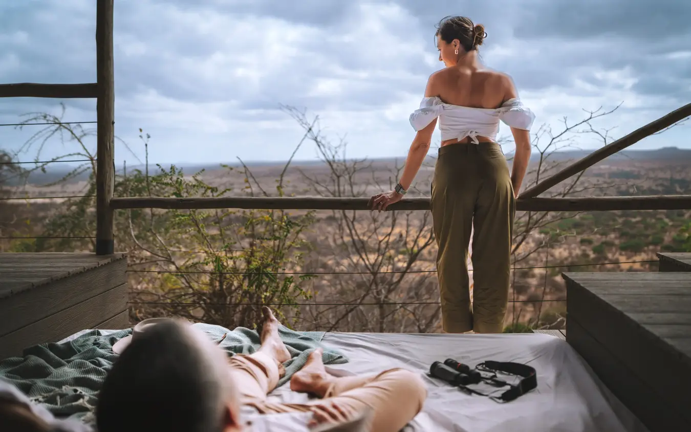 Couple relaxing on bed with savanna valley vista from open-air platform, Mpingo Ridge Lodge, Tarangire National Park, Tanzania