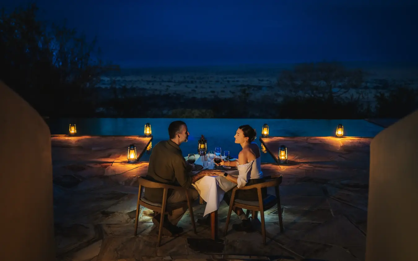 Couple dining at table on sandy terrain at dusk with lantern lighting, Mpingo Ridge Lodge, Tarangire National Park, Tanzania