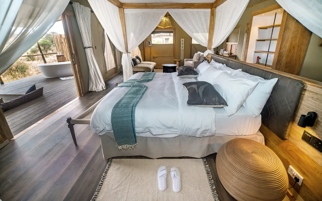 Luxury safari tent bedroom with draped canopy and private deck overlooking landscape, Mpingo Ridge Lodge, Tarangire National Park, Tanzania