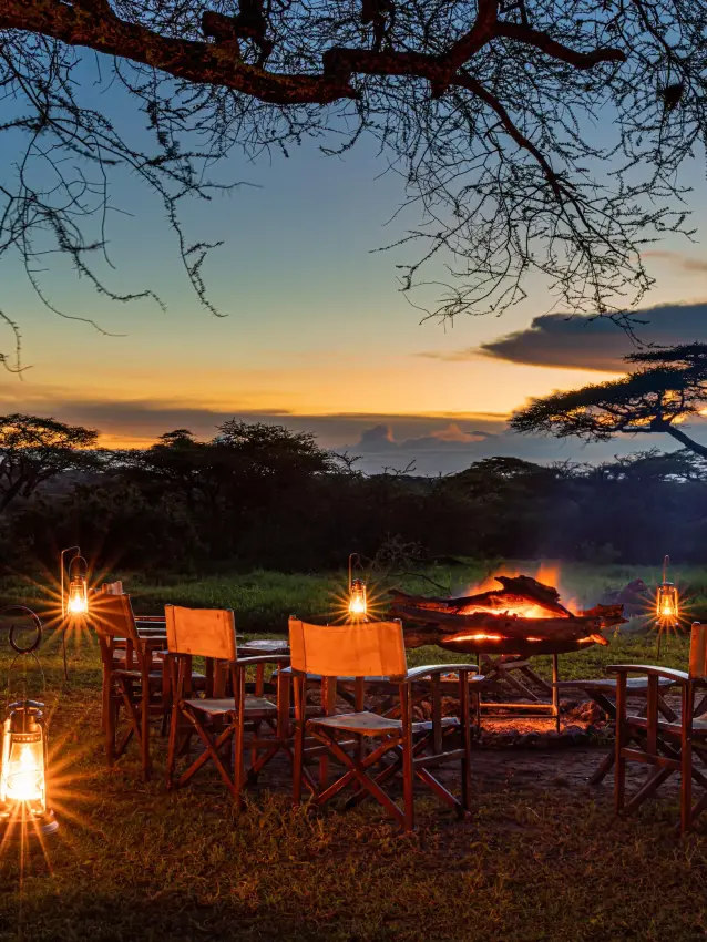 Evening dining setup with fire under acacia trees at sunset, Lemala Ngorongoro, Ngorongoro Crater, Tanzania