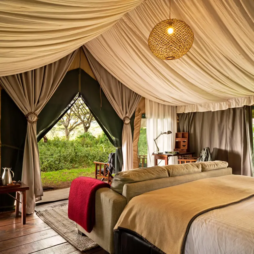 Luxury tent bedroom with draped fabric and garden views, Lemala Ngorongoro, Ngorongoro Crater, Tanzania