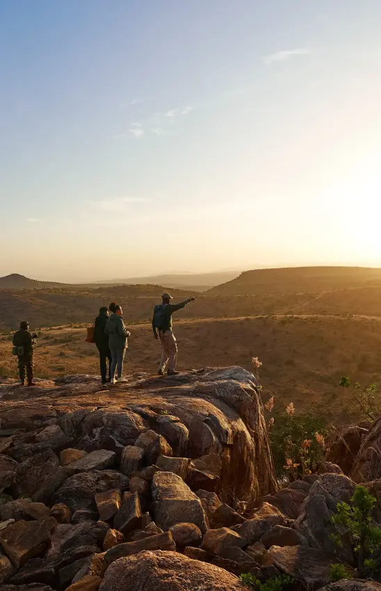 Guests standing on rocky outcrop at sunset overlooking savanna, Lengishu House, Laikipia Highlands, Kenya