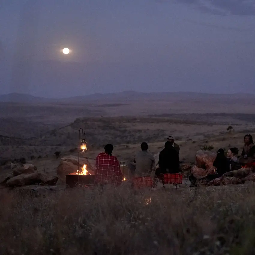 Guests gather around campfire under moonlit desert sky, Lengishu House, Laikipia Highlands, Kenya