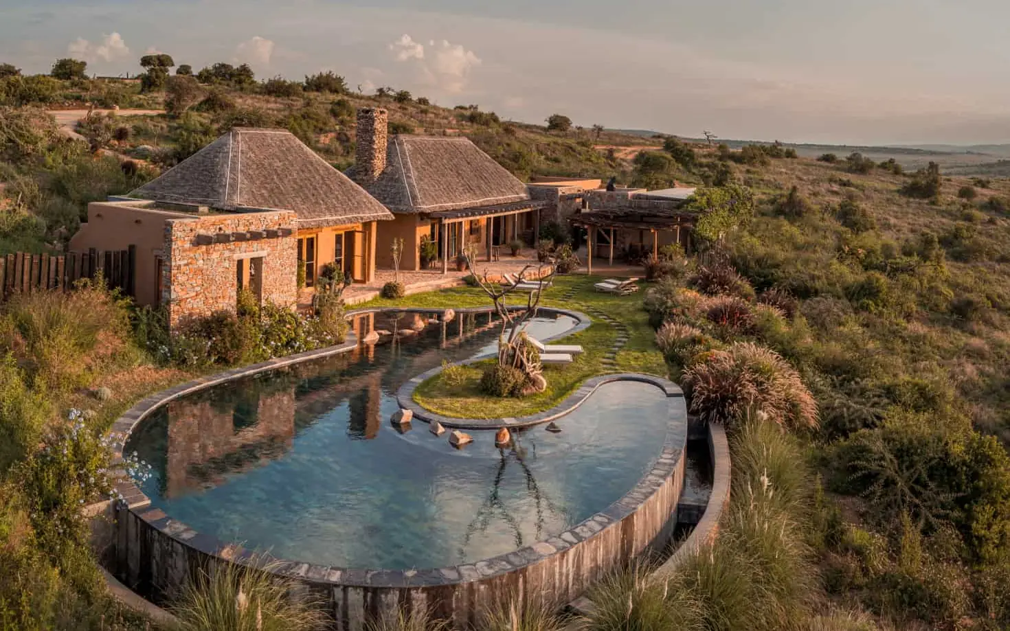 Curved swimming pool with guests surrounded by savanna landscape, Lengishu House, Laikipia Highlands, Kenya