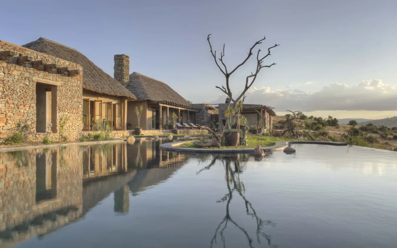 Infinity pool reflecting stone lodge building at sunset, Lengishu House, Laikipia Highlands, Kenya