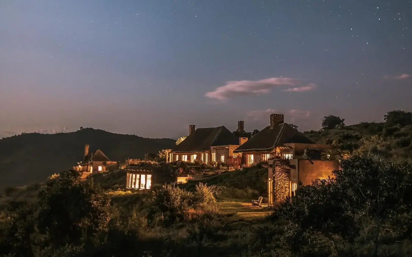 Illuminated stone lodge buildings nestled in twilight landscape, Lengishu House, Laikipia Highlands, Kenya