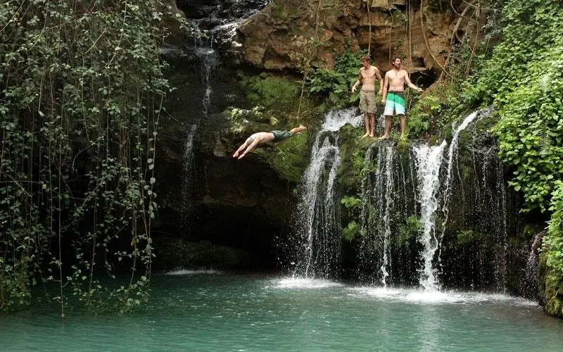 Guests diving and swimming at tropical waterfall pool, Lengishu House, Laikipia Highlands, Kenya