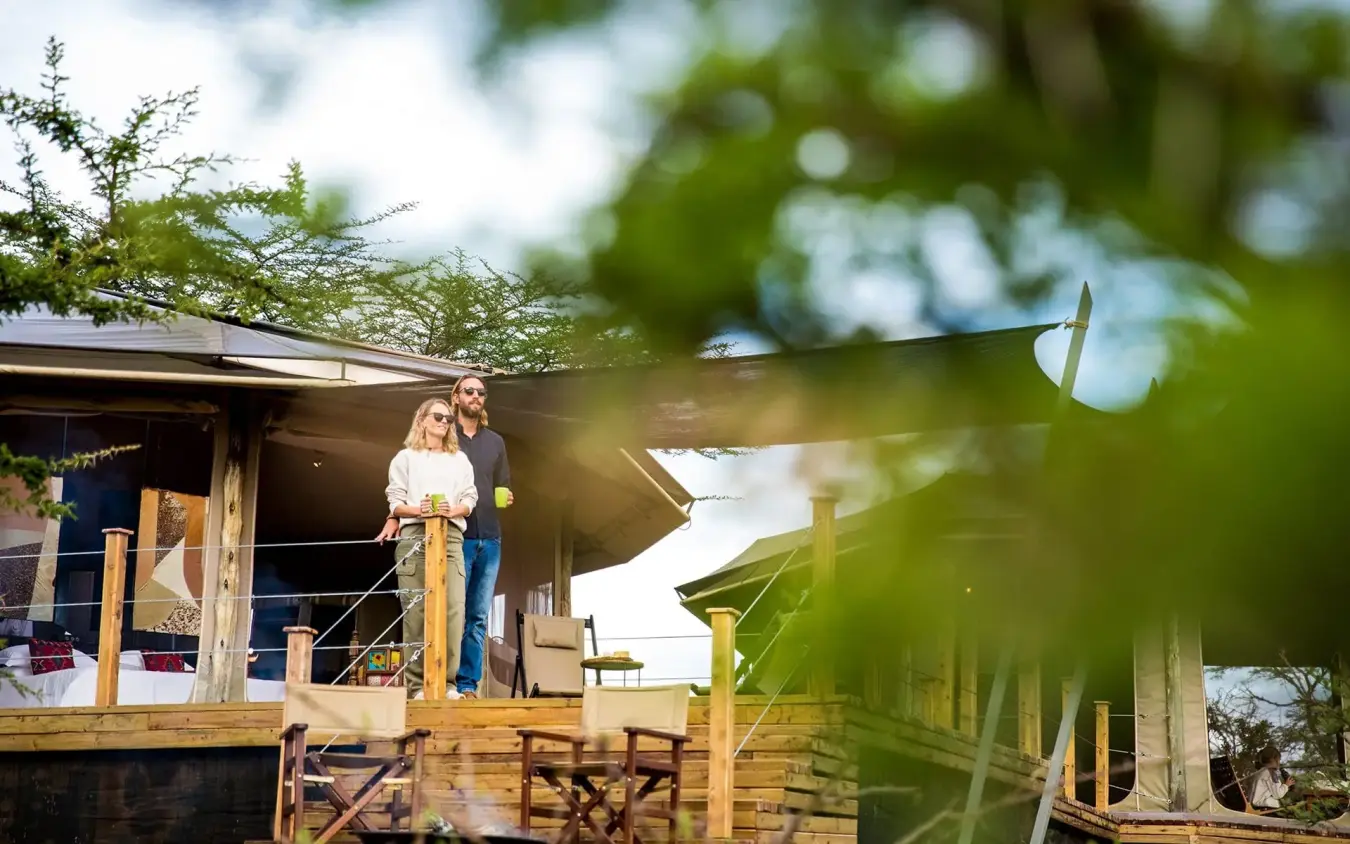 Couple standing on wooden deck of safari lodge with savanna views, Leopard Hill, Maasai Mara, Kenya