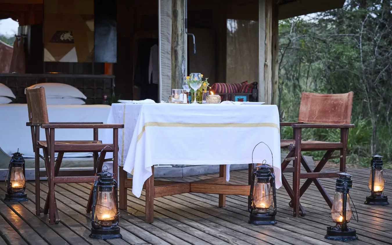 Outdoor dining setup on wooden deck with lanterns and forest backdrop, Leopard Hill, Maasai Mara, Kenya