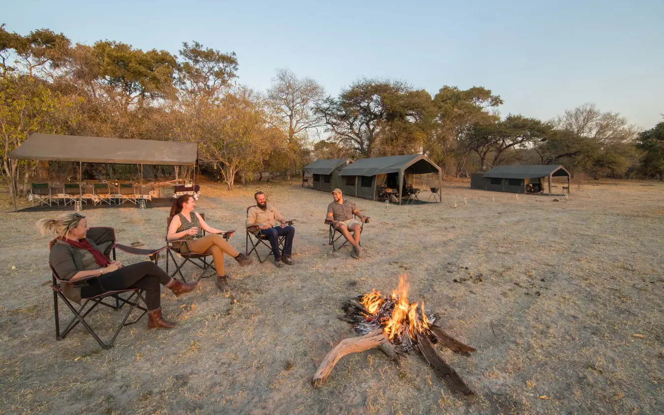 Guests gathered around campfire at safari camp at sunset
