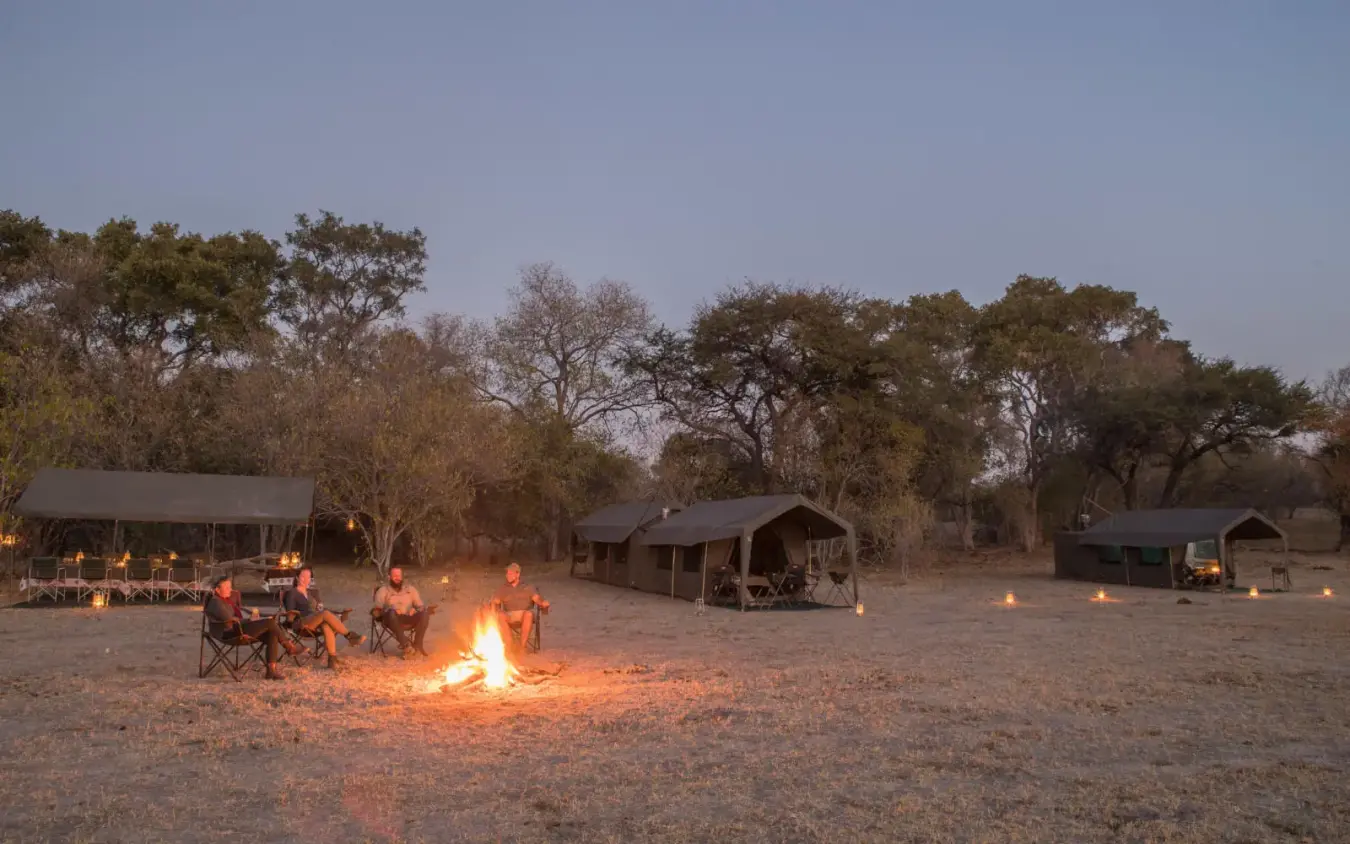 Guests gathered around campfire at dusk in safari camp